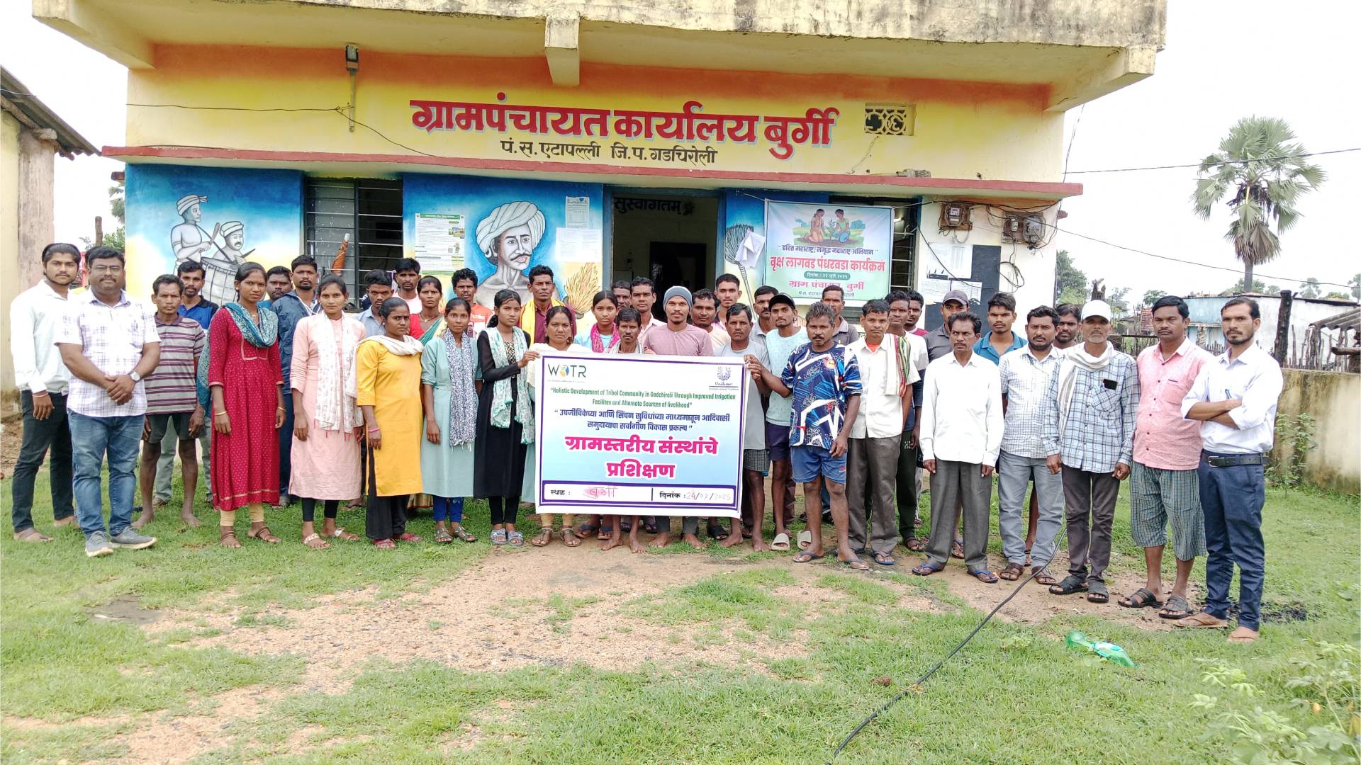 Group of people standing in front of a building with a banner in a rural area credit to Watershed Organisation Trust
